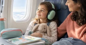 Enfant portant un casque anti-bruit vert menthe près du hublot d’un avion, accompagné d’un parent